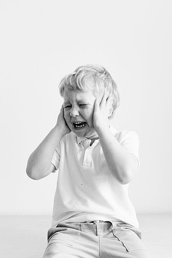 Black and white portrait of a sad child covering ears, expressing frustration. HD phone wallpaper