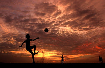 A child playing soccer on the beach at sunset in Kochi, India, creating a striking silhouette against the vibrant sky. HD wallpaper