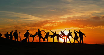 Group of people silhouetted against a vibrant sunset, showcasing unity and joy. HD wallpaper