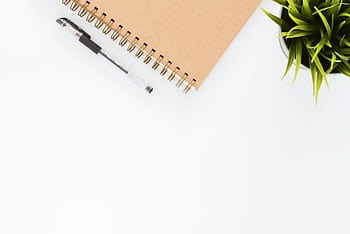 Minimalist stationery setup with a spiral notebook and pen on a clean white desk. HD wallpaper