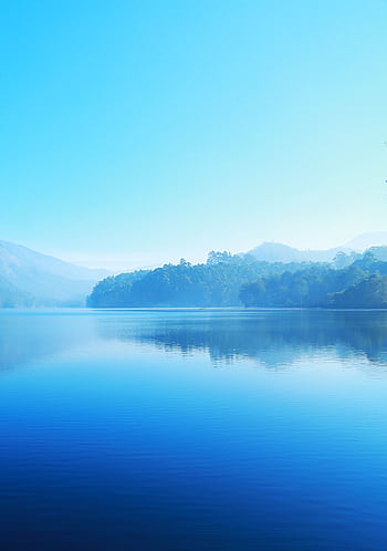 A tranquil lake reflecting misty mountains under a bright blue sky, offering a sense of calm and serenity. HD phone wallpaper