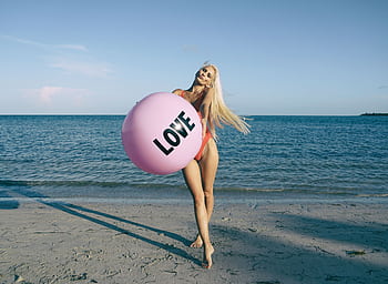 A joyful adult woman playing with a large pink ball on a sunny Miami beach. HD wallpaper