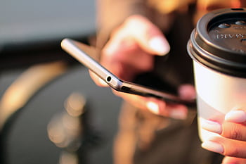 Person holding a smart and a takeaway coffee cup while texting outdoors. HD wallpaper