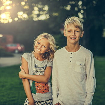 A joyful brother and sister smiling outdoors in a sunlit garden. Perfect stock for family and lifestyle themes. HD phone wallpaper