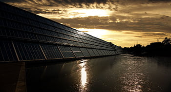Silhouetted solar panels reflect sunset in tranquil waters, showcasing renewable energy. HD wallpaper