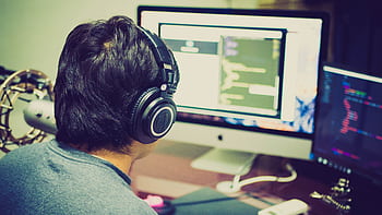 A programmer with heads focuses on coding at a computer setup with dual monitors. HD wallpaper