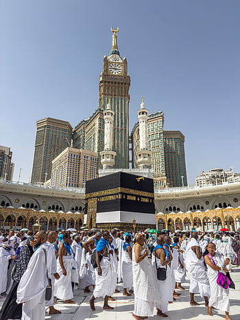A large group of pilgrims gather at the Kaaba in Mecca, Saudi Arabia, during the Hajj pilgr under a clear blue sky. HD phone wallpaper