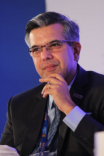 Portrait of a thoughtful businessman in a suit, wearing eyeglasses, captured in an indoor corporate setting. HD phone wallpaper