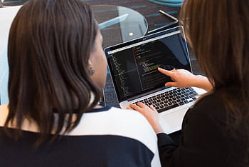 Two women working together on software programming indoors, focusing on code. HD wallpaper