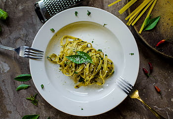 A tempting plate of basil pesto pasta garnished with cheese, surrounded by fresh ingredients. HD wallpaper