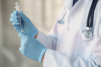 Healthcare professional wearing gloves and holding a syringe in a clinical setting. HD wallpaper