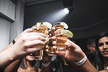 Friends raising tequila shots with lime in a lively indoor bar setting. HD wallpaper