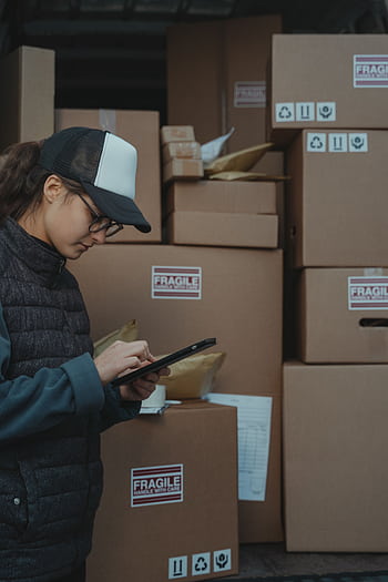 A warehouse employee checks inventory on a tablet beside stacked boxes marked fragile. HD phone wallpaper