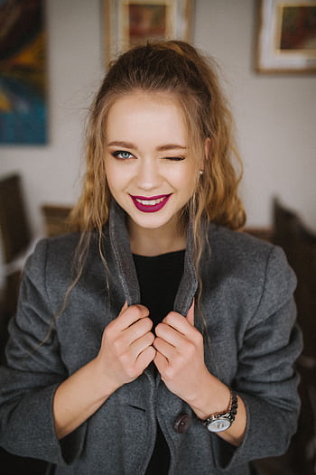 Charming young woman with red lips and casual grey coat winking indoors. HD phone wallpaper