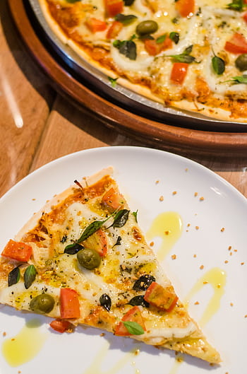 Close-up of a delicious pizza slice with toppings like cheese, olives, and tomatoes on a white plate. HD phone wallpaper