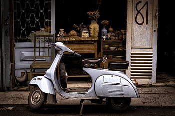 A classic Vespa scooter parked in front of a charming café, evoking retro vibes. HD wallpaper