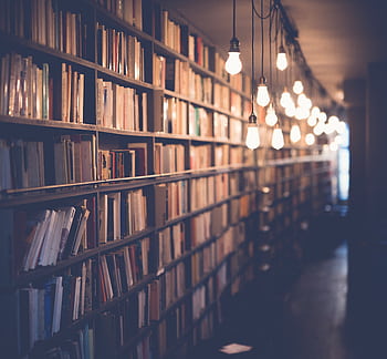 Rows of bookshelves in a cozy library with warm ambient lighting. Perfect for learning and knowledge themes. HD wallpaper