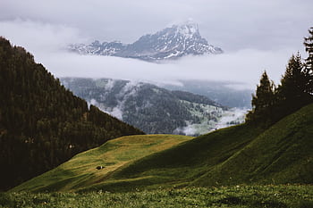 Breath-taking mountain landscape with lush green hills and misty valleys under a cloudy sky. HD wallpaper