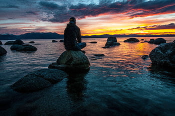 Silhouette of a man seated on rocks, gazing at a serene Lake Tahoe sunset. HD wallpaper