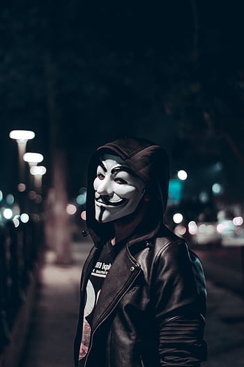 A person wearing a Guy Fawkes mask poses on a dimly lit urban street at night. HD phone wallpaper