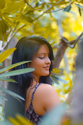 A serene portrait of a woman amidst lush green foliage in daylight. HD phone wallpaper