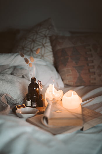 A warm and cozy bedroom scene with burning candles, a book, and essential oils creating a relaxing atmosphere. HD phone wallpaper