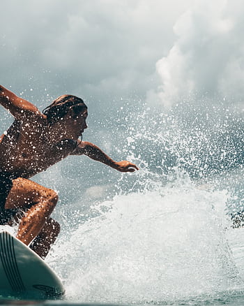 Energetic surfer rides ocean waves in tropical Indonesia, capturing the thrill of water sports. HD phone wallpaper