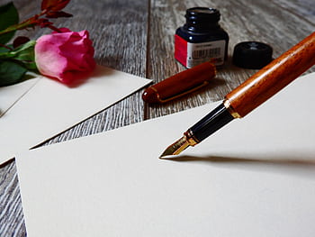 A romantic setup with a rose, fountain pen, and paper, perfect for heartfelt writing. HD wallpaper