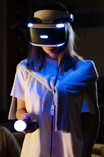 A young woman immersed in virtual reality gaming, wearing a VR headset and controller. HD phone wallpaper