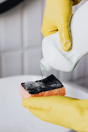 Close-up of hands in yellow gloves pouring detergent on sponge, showcasing cleaning process. HD phone wallpaper