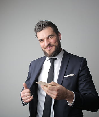Smiling businessman in formal attire holding a card, exuding confidence in a studio portrait. HD phone wallpaper