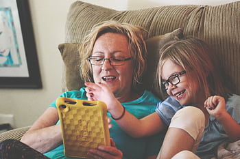 A joyful grandmother and grandchild bonding over a tablet on a cozy sofa indoors. HD wallpaper