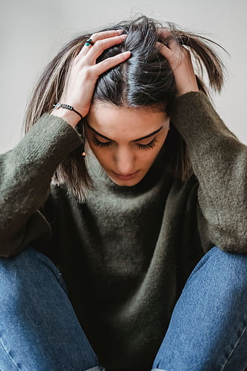 A woman sitting indoors, appearing stressed or upset, touching her head. HD phone wallpaper