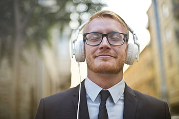 Portrait of a young man in a suit, wearing heads and enjoying music outdoors with a blurred urban background. HD wallpaper