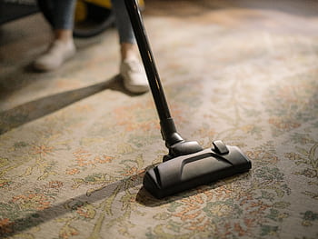 Close-up of a vacuum cleaner on a patterned carpet in a sunlit room, capturing a moment of household cleaning. HD wallpaper