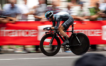 Dynamic shot of a cyclist competing in a fast-paced cycling event, showcasing speed and athleticism. HD wallpaper