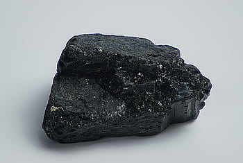 Detailed macro shot of a black mineral rock on a plain surface, showcasing texture and natural form. HD wallpaper