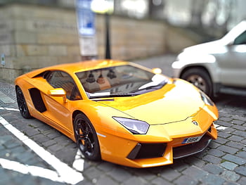 Yellow sports car on a cobblestone street, showcasing sleek design and vibrant color. HD wallpaper