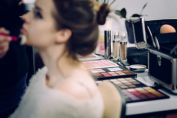 A woman receiving professional makeup in a studio with various cosmetics in focus. HD wallpaper