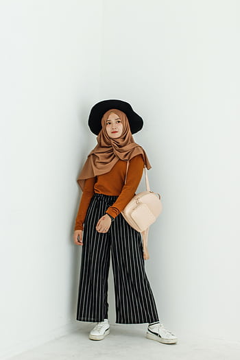 Fashionably dressed woman in hijab posing against a minimalist white wall, showcasing a stylish look. HD phone wallpaper