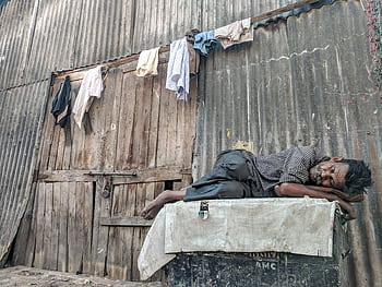 An elderly man peacefully sleeps against a rundown wooden wall with hanging clothes. HD wallpaper