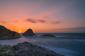 Captivating sunset over a rocky seascape with vibrant colors and gentle waves. HD wallpaper