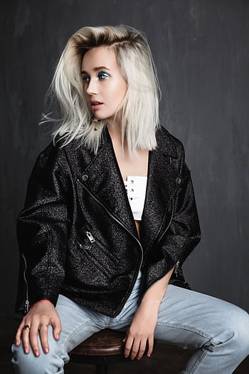 A fashionable young woman with blonde hair wearing a trendy jacket poses confidently indoors. HD phone wallpaper