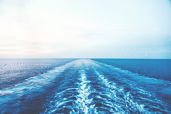 Serene ocean view with a deep blue wake against a light sky, evoking calm and infinity. HD wallpaper
