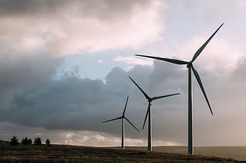 Wind turbines generating renewable energy under a dramatic cloudy sky. HD wallpaper