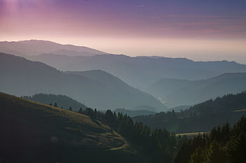 A beautiful view of rolling hills and forests under a colorful sunset sky. HD wallpaper