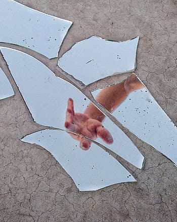 A hand reaching out is reflected in scattered pieces of a broken mirror on a textured surface. HD phone wallpaper