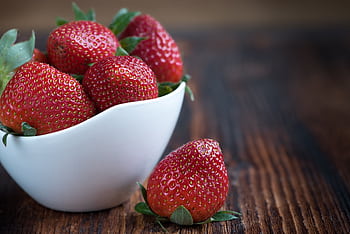 Close-up of fresh strawberries in a white bowl on a rustic wooden table, highlighting vibrant red color. HD wallpaper