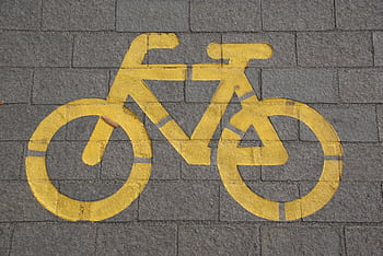 Bright yellow bicycle symbol on gray pavement marking a bike lane. HD wallpaper