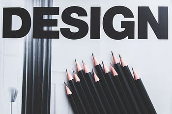 Black pencils arranged creatively next to large typography 'DESIGN'. HD wallpaper